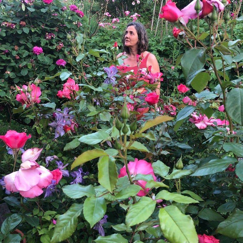Frau steht mitten im Rosengarten
