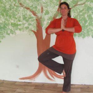 Frau steht in der yogaasana der Baum vor einem gemalten Baum auf einer Wand. 