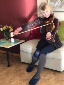 Eine Frau Sitz auf einem Hocker und spielt hingebungsvoll Geige 